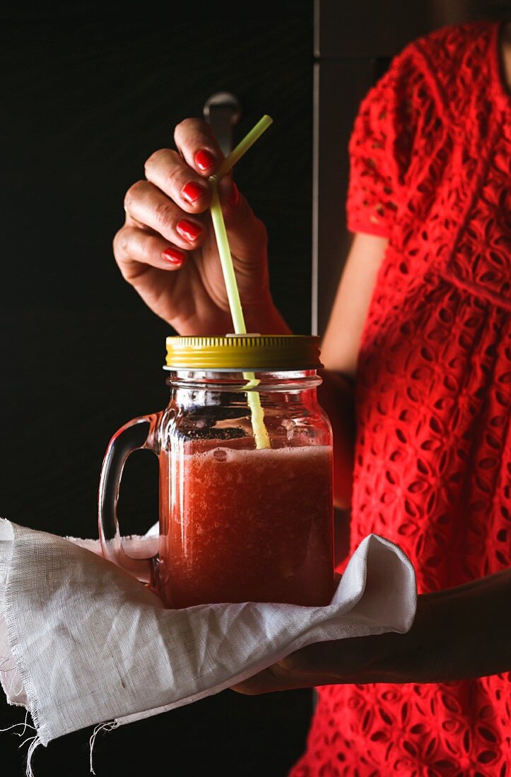A woman holding a smoothie in a screw-top jar with a straw