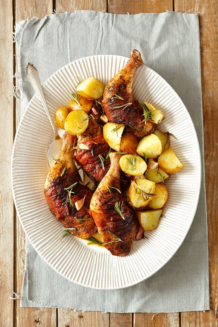 Oven-roasted chicken legs wrapped in ham with potatoes