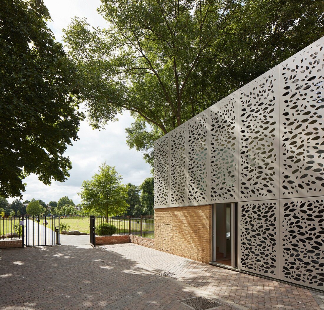 Building with modern perforated façade elements, paved courtyard and view into park-style gardens