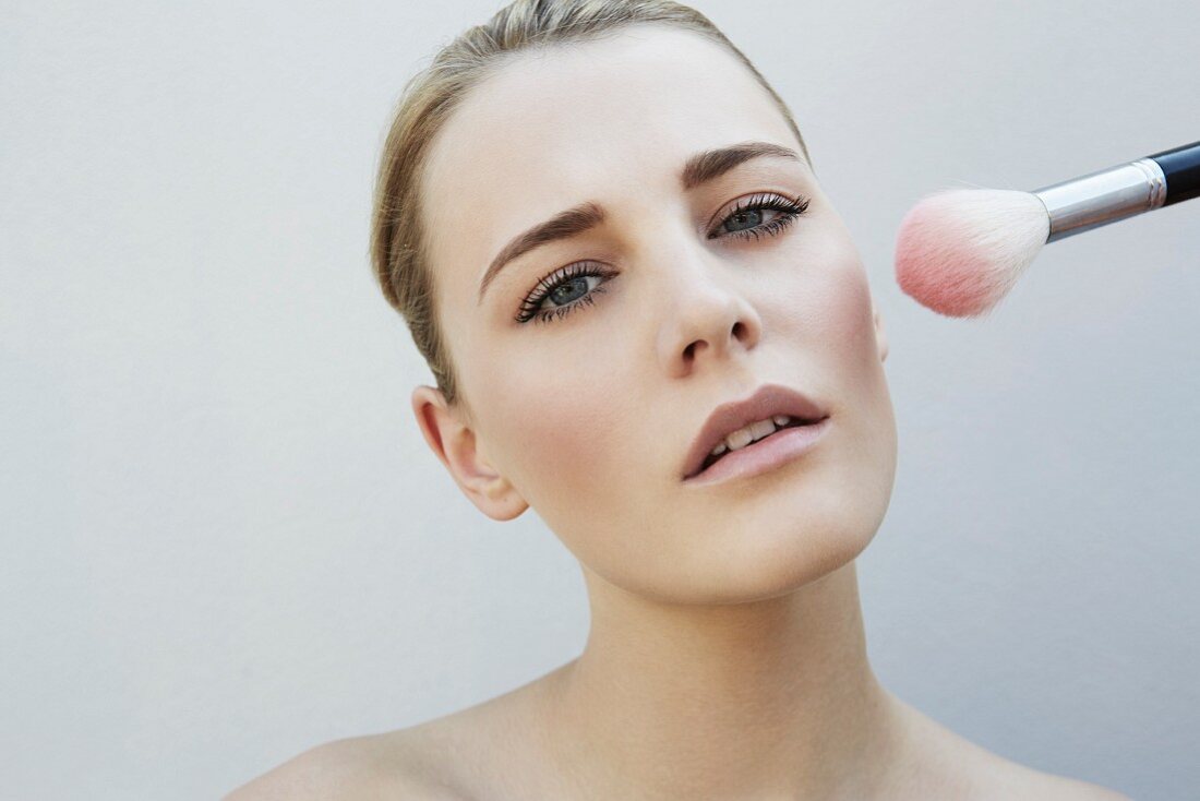 A young blonde woman with a blusher brush next to her cheek