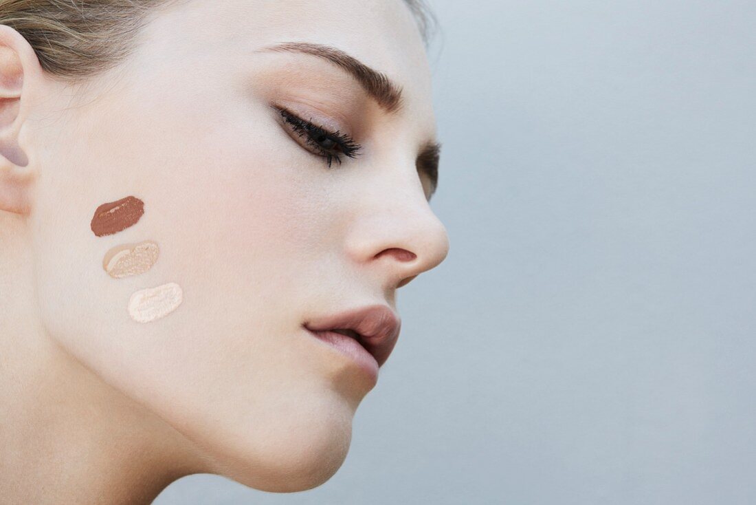 A young blonde woman with different make-up samples on her cheek