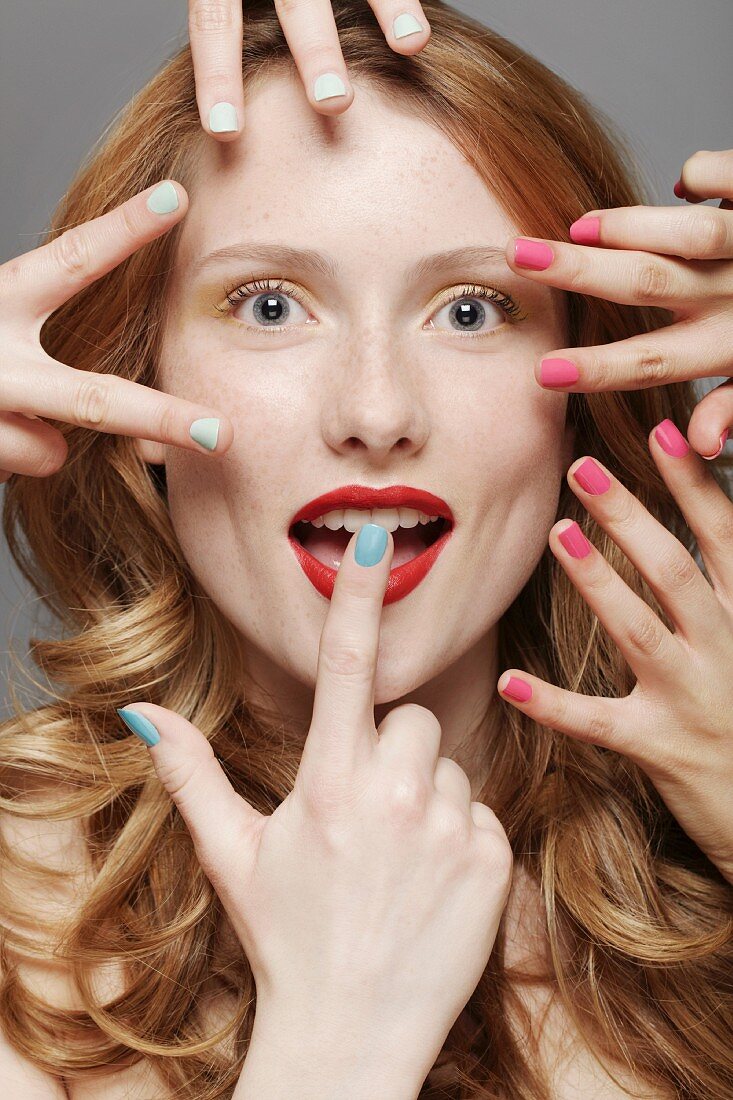 A red-haired woman surrounded by several hands wearing different coloured nail varnishes