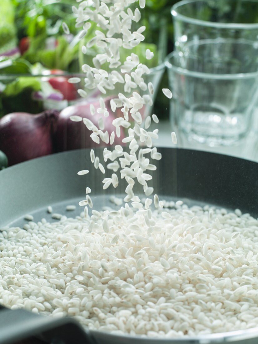Risotto rice being sprinkled into a pan
