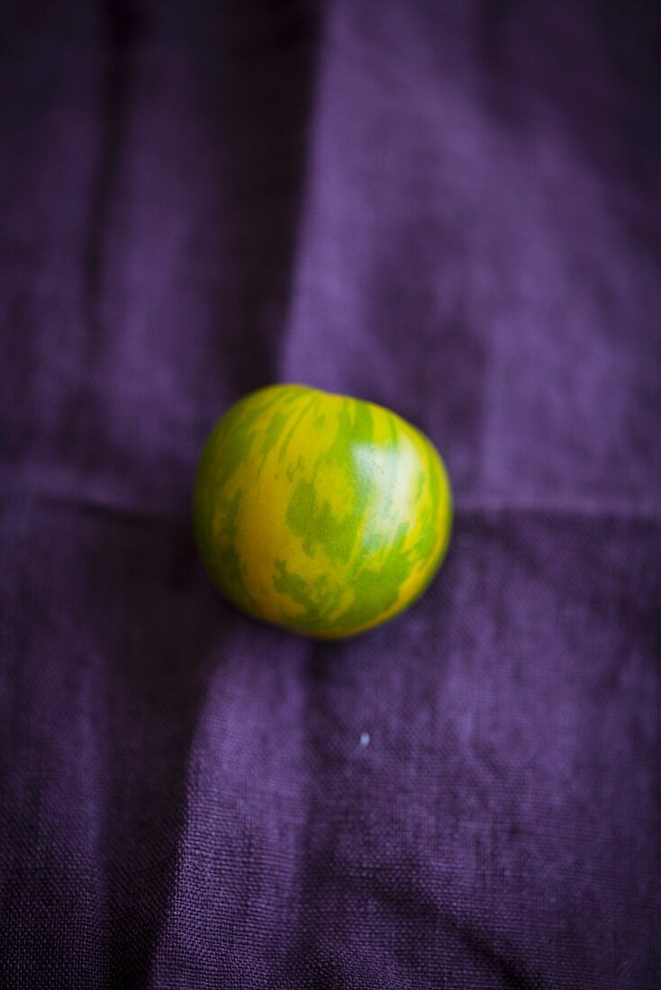 Eine grüne Zebratomate auf violettem Tuch