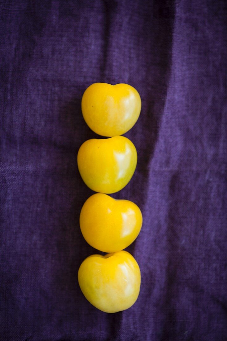 Vier gelbe Tomaten auf violettem Tuch