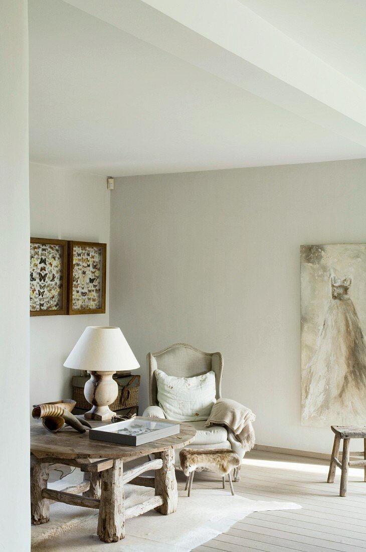 Rustic solid-wood table on animal-skin rug next to antique wing-back chair and painting