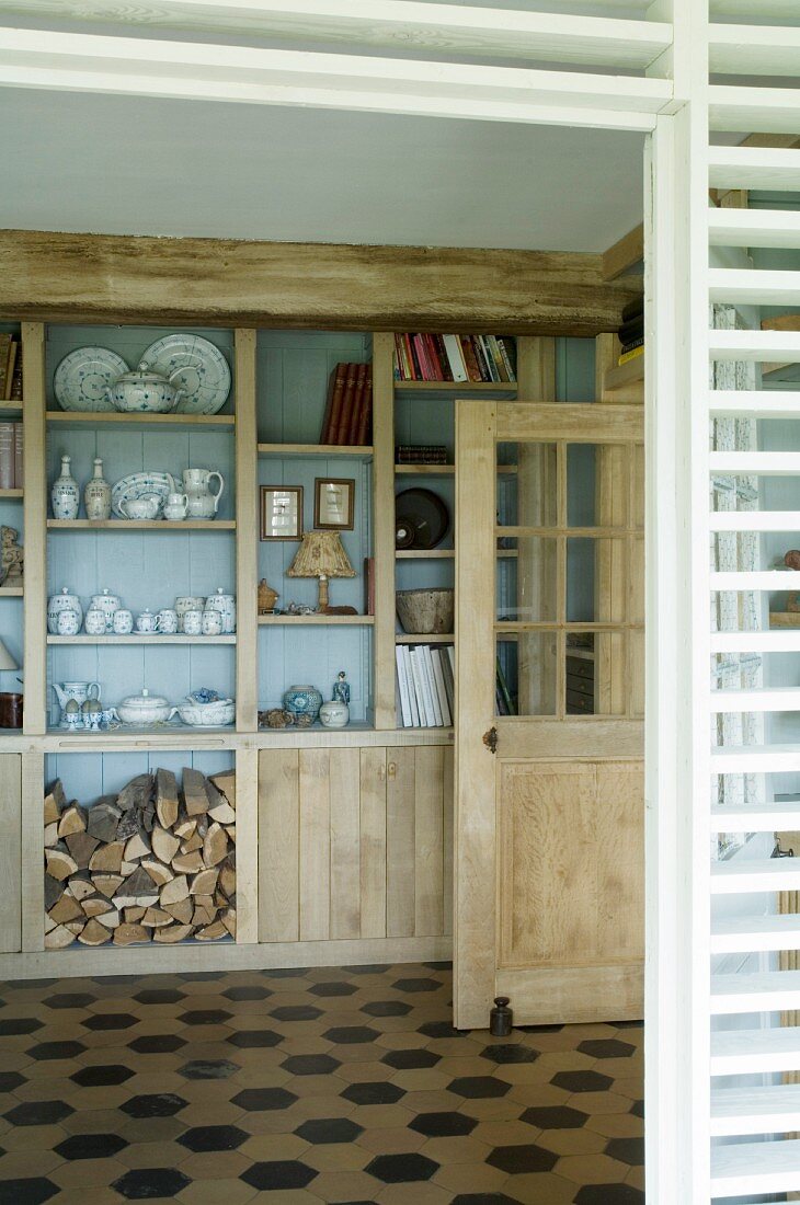 Glasses, books and firewood on fitted shelves in renovated country house