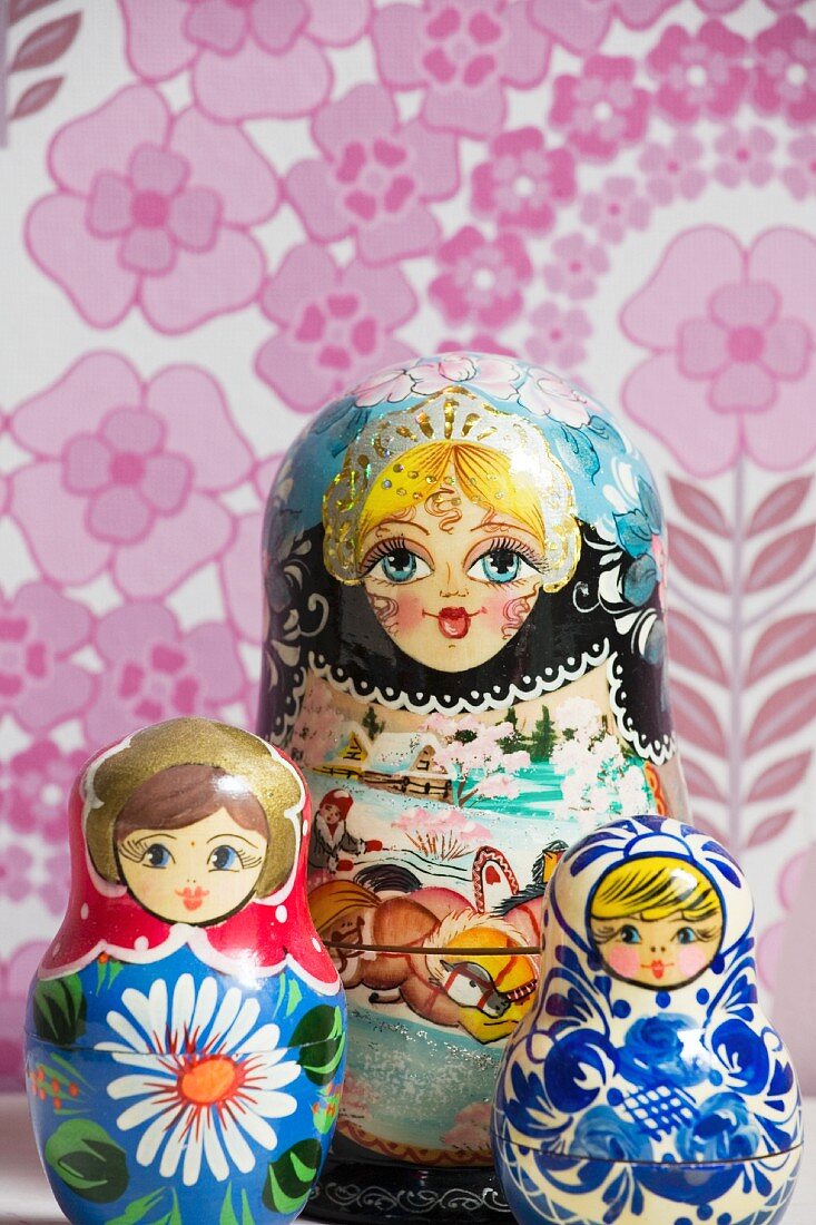 Three Russian dolls in front of pink floral wallpaper