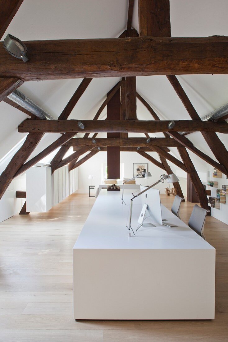 Rustic roof beams and white designer desk in converted attic