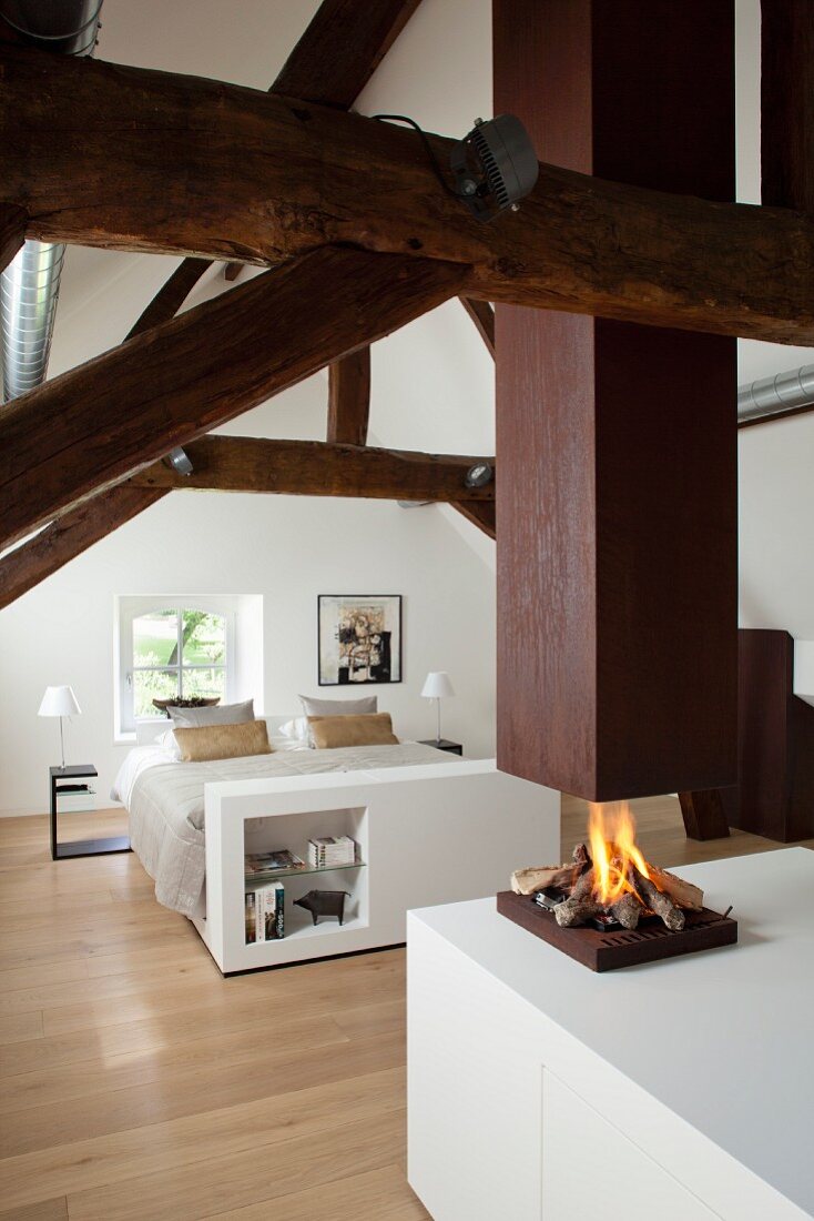 Elegantes weißes Dachgeschoss-Schlafzimmer mit restaurierter Fachwerkkonstruktion und offener Feuerstelle unter Kaminabzug