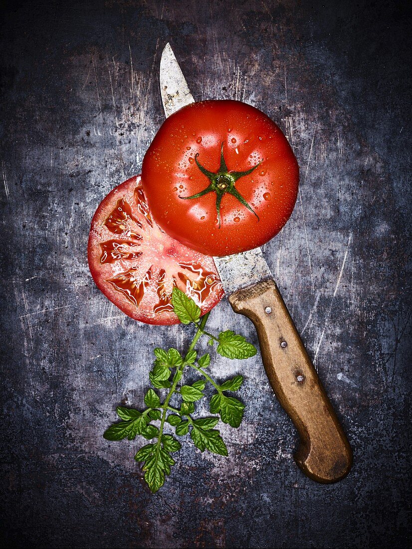 A beef tomato sliced in half with a knife on a grey surface (seen from above)