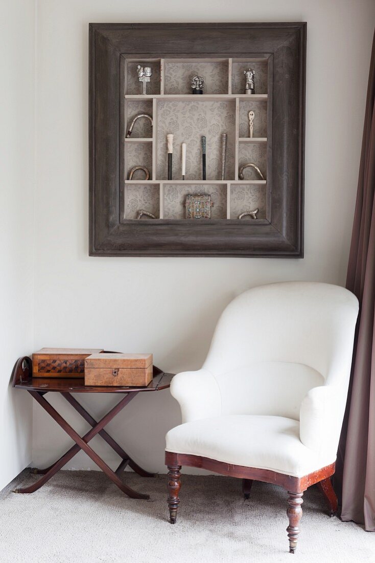 White antique armchair and side table below collection of walking-stick handles in display case