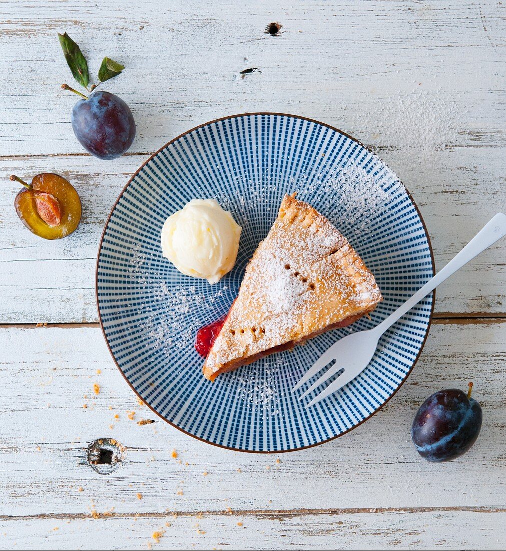 A slice of plum pie on a plate with a scoop of ice cream