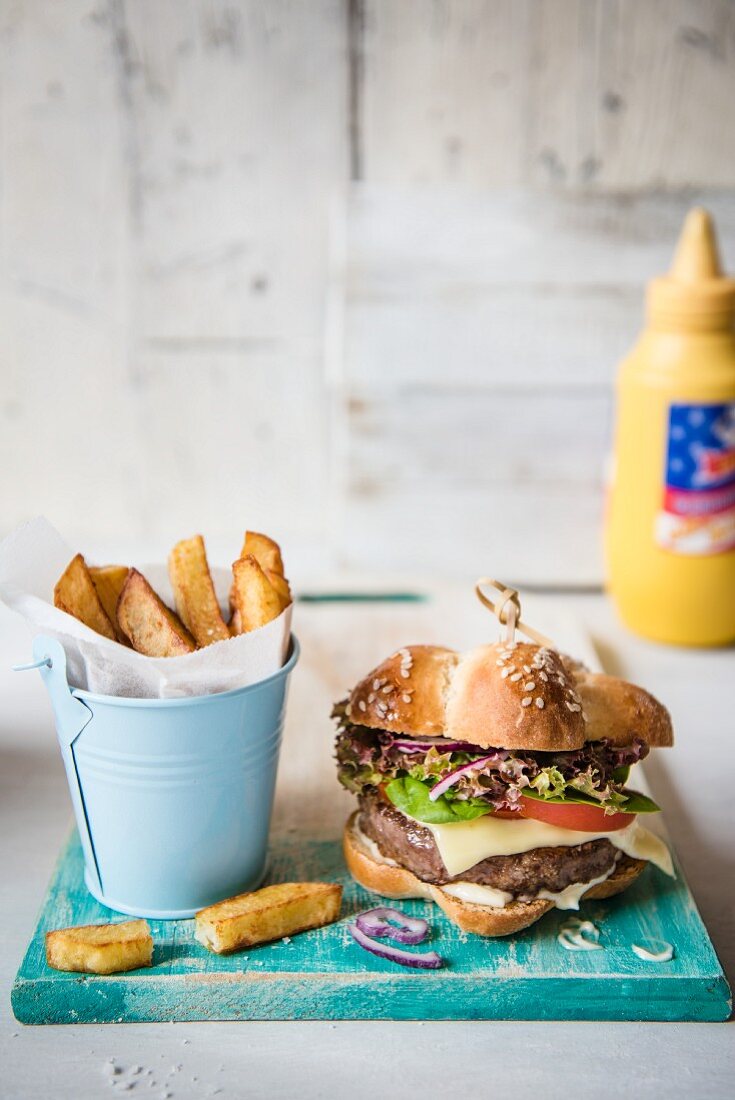 A cheeseburger with chips in front of a bottle of mustard