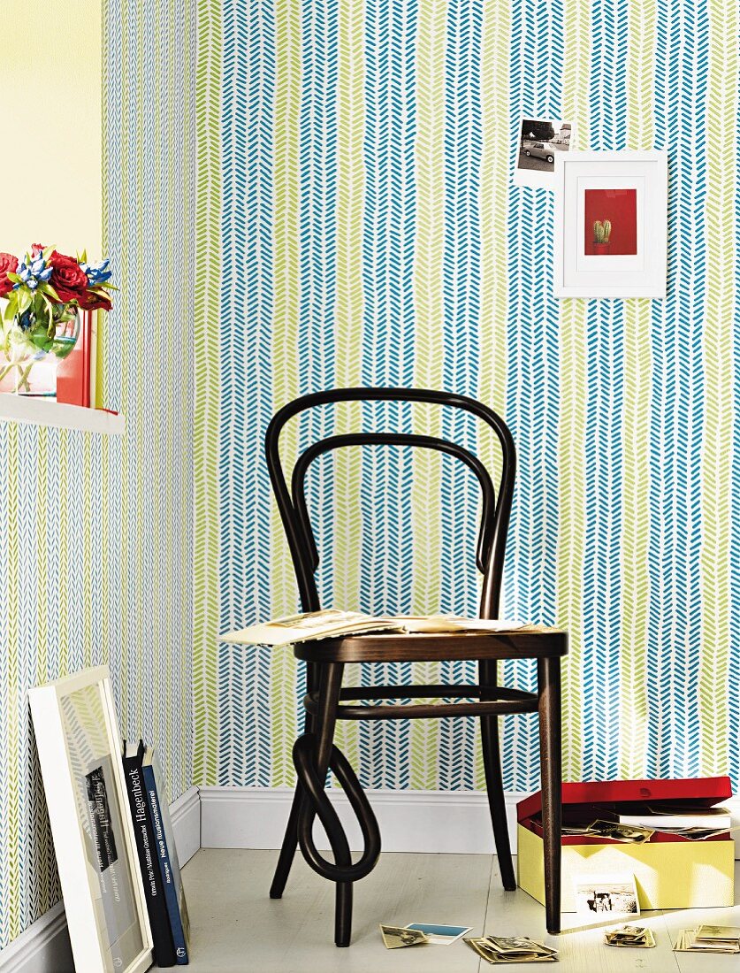 A wooden Thonet-style chair with a photo album and photo box on the floor in front of green and blue non-woven wallpaper with a fishbone pattern