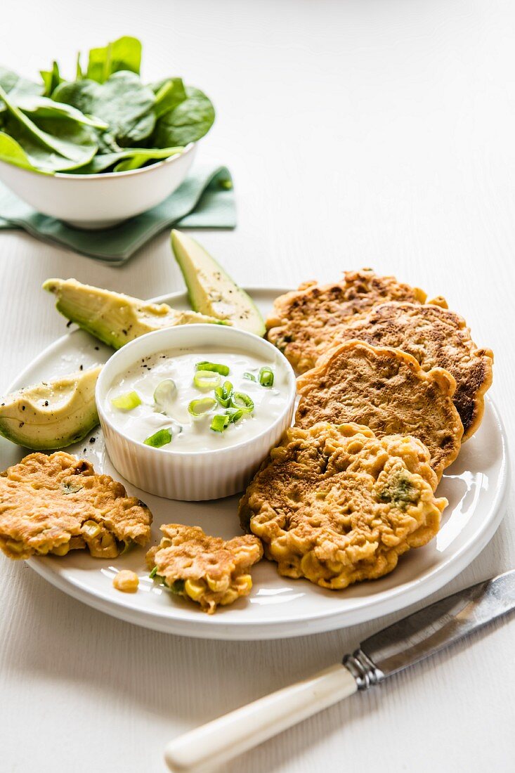 Corn friters on a plate with sour cream & onion dip and avocado