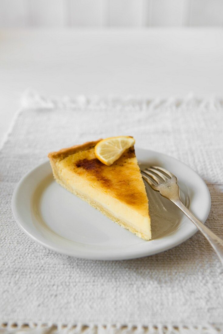 A slice of lemon tart on a plate with a fork