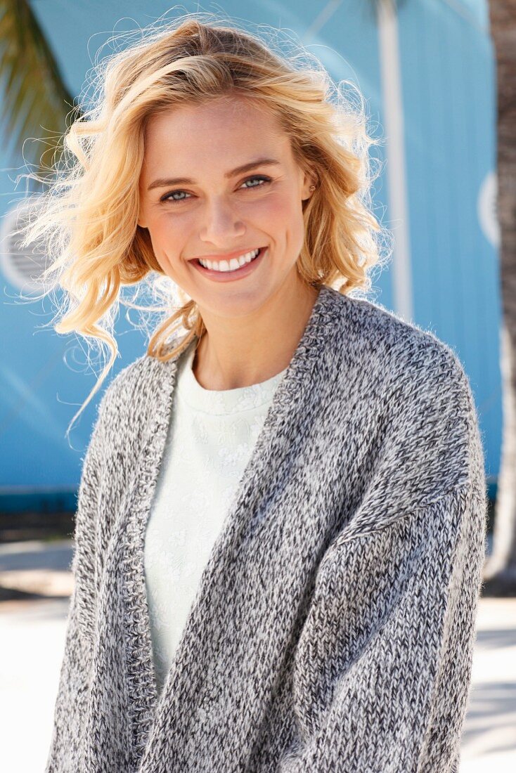 A young blonde woman in a white top and mottled grey knitted cardigan