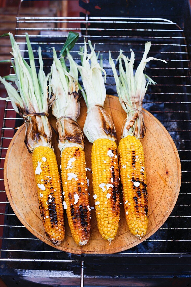 Grilled corn on the cob on a wooden plate