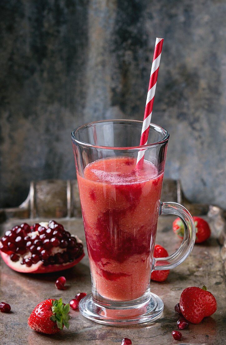 A glass of strawberry & pomegranate smoothie with a straw and fresh berries