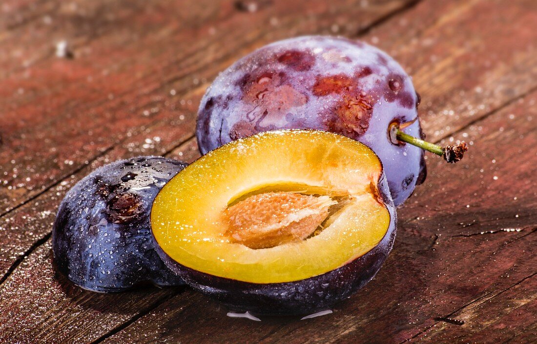 Whole and halved plums on a wooden surface