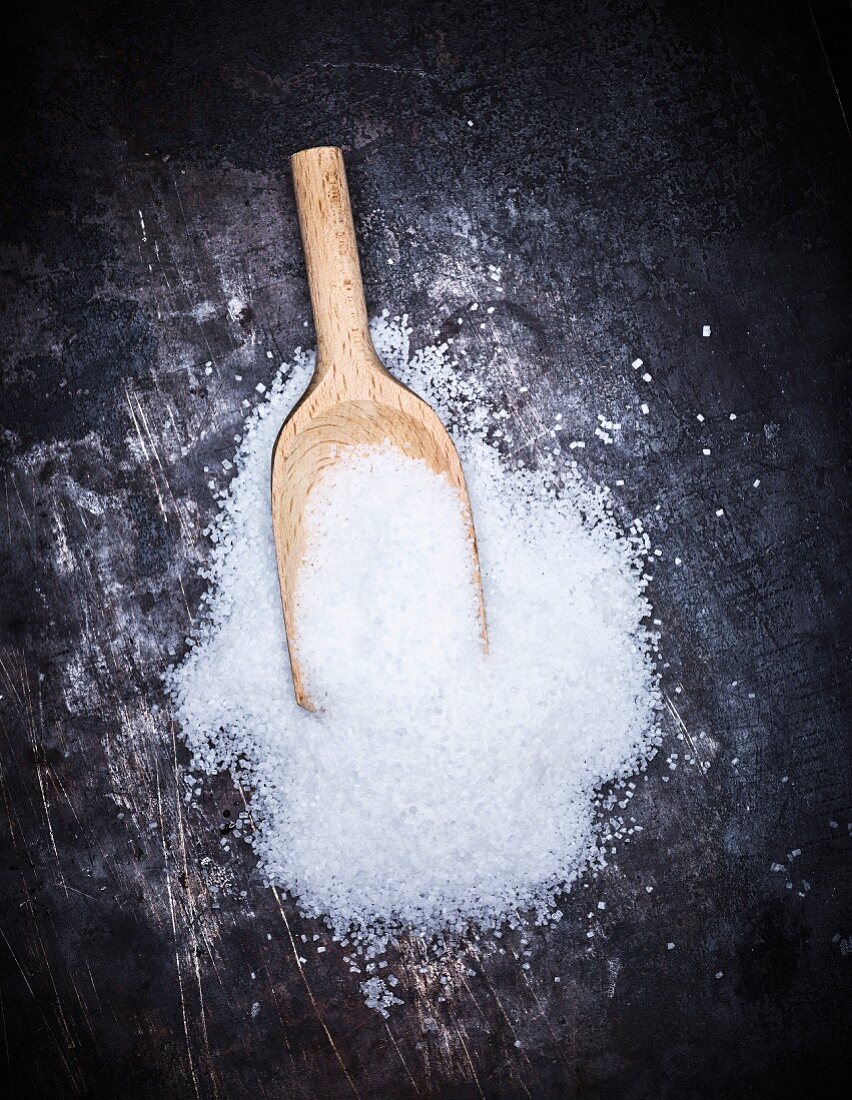 A pile of sugar with a wooden scoop