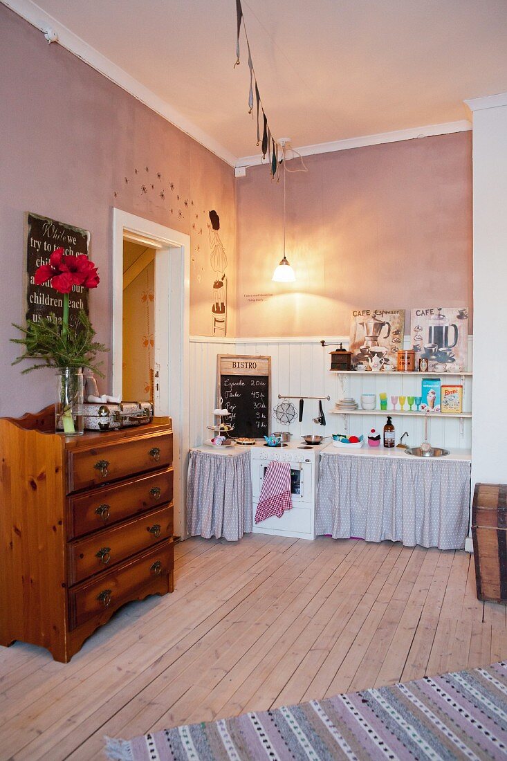 Vintage play kitchen against white wooden cladding, wooden floor and chest of drawers