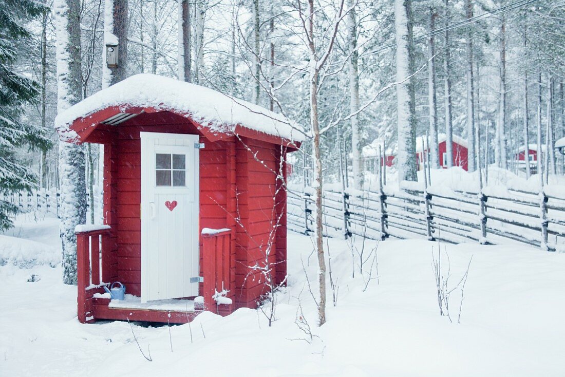 Kleines rotes Holzhaus im verschneiten Wald
