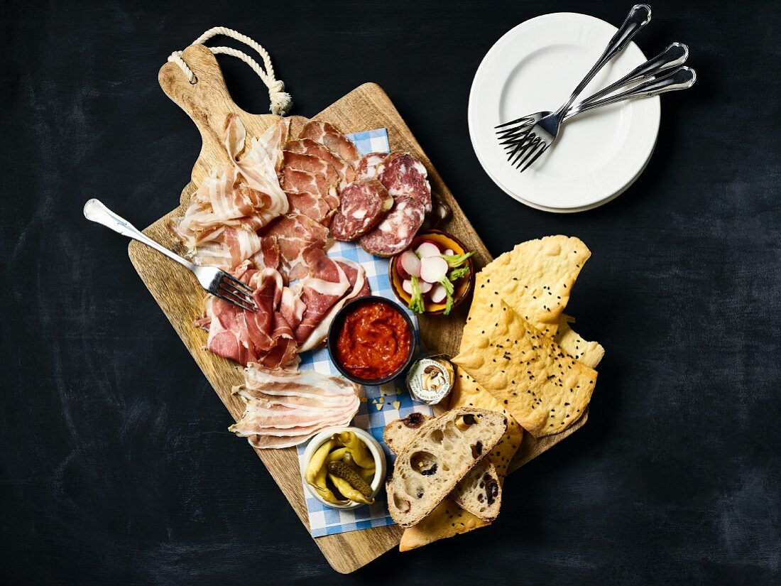 A charcuterie platter with bread, radishes and gherkins (seen from above)