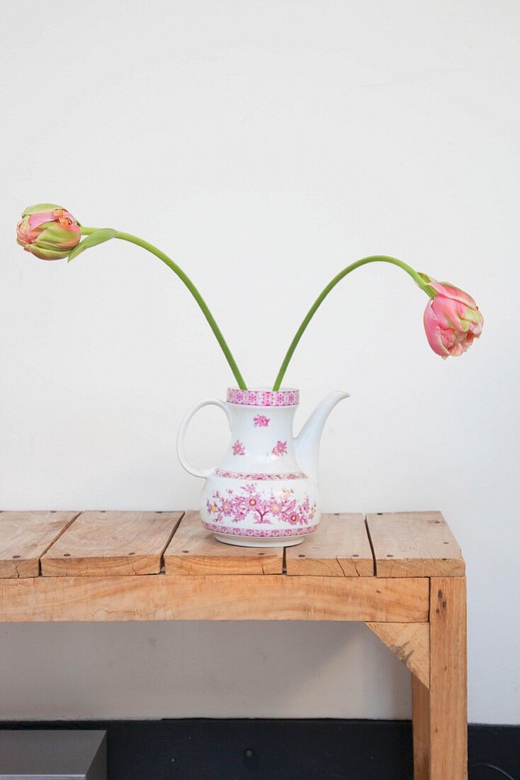 Two tulips in retro coffee pot on rustic wooden bench