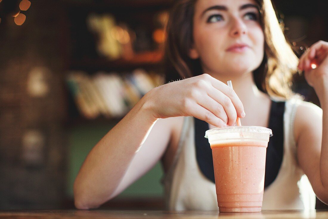 Junge Frau trinkt einen Smoothie in einer Kaffeebar