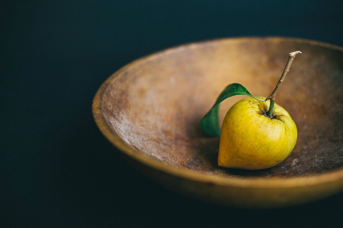 A fresh lemon with a stem in a wooden bowl