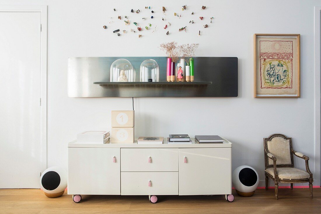 Retro sideboard on castors next to antique armchair below artistic wall decorations