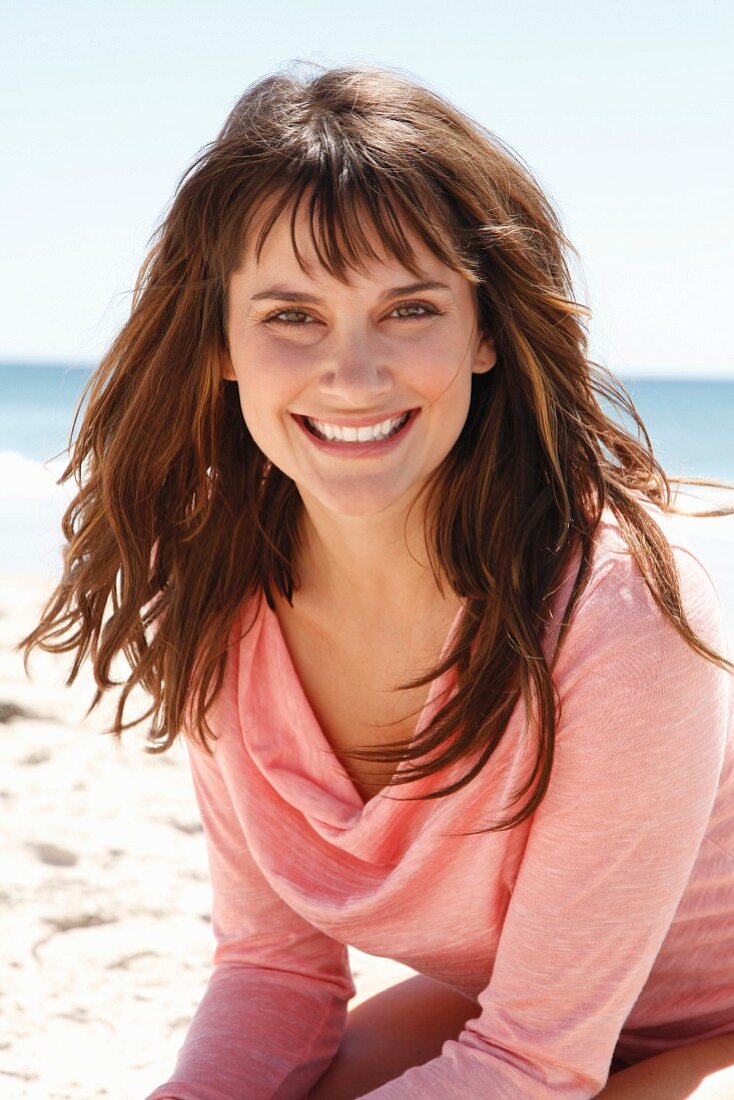 A brunette woman in a pink long-sleeved top on the beach