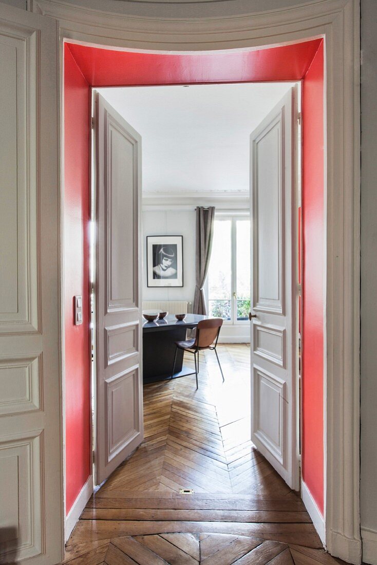 View through red door frame and open panelled double doors into dining room of period apartment