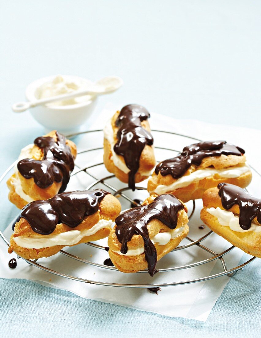 Chocolate eclairs filled with cream on a cooling rack