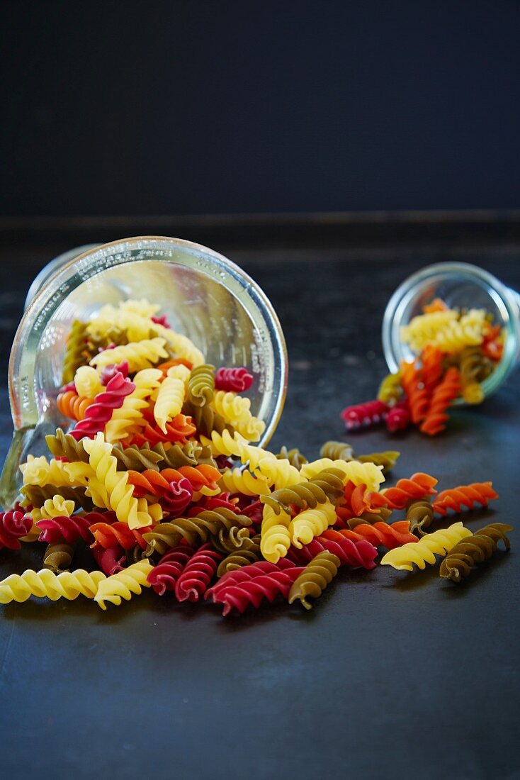 Colourful fusilli pasta in a measuring cup and a glass on their side