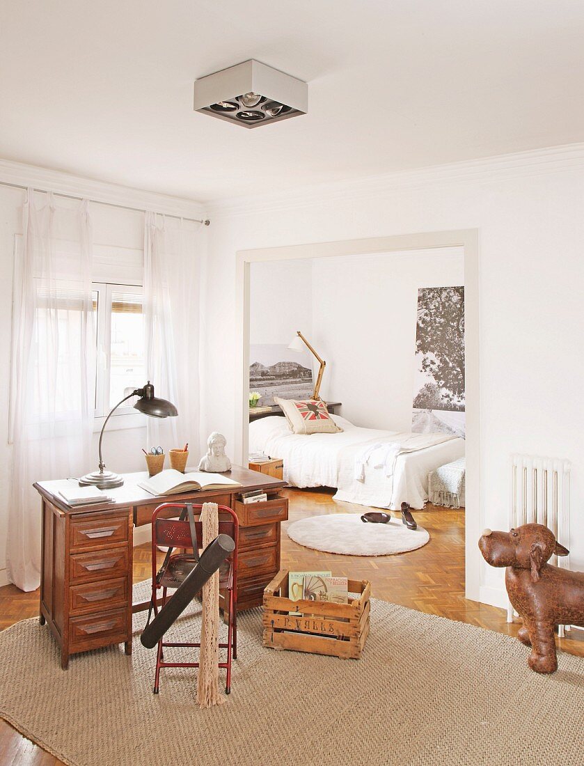 Table lamp on retro desk and metal chair on rug with view into bedroom through open doorway