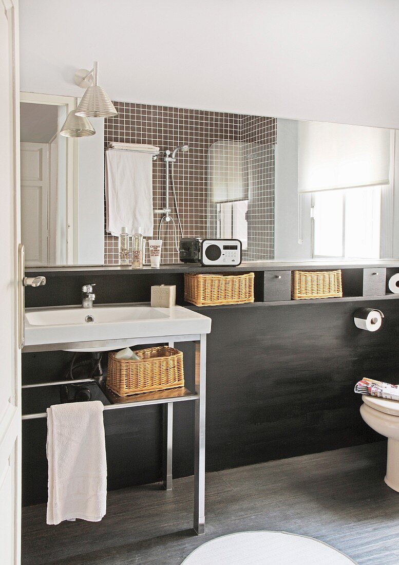 Bad mit Waschtisch vor schwarzer Ablagefläche mit Aufbewahrungskörbchen und Wandspiegel