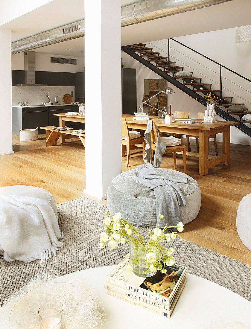 Long dining table and kitchen counter below steel staircase in loft apartment with lounge area in foreground