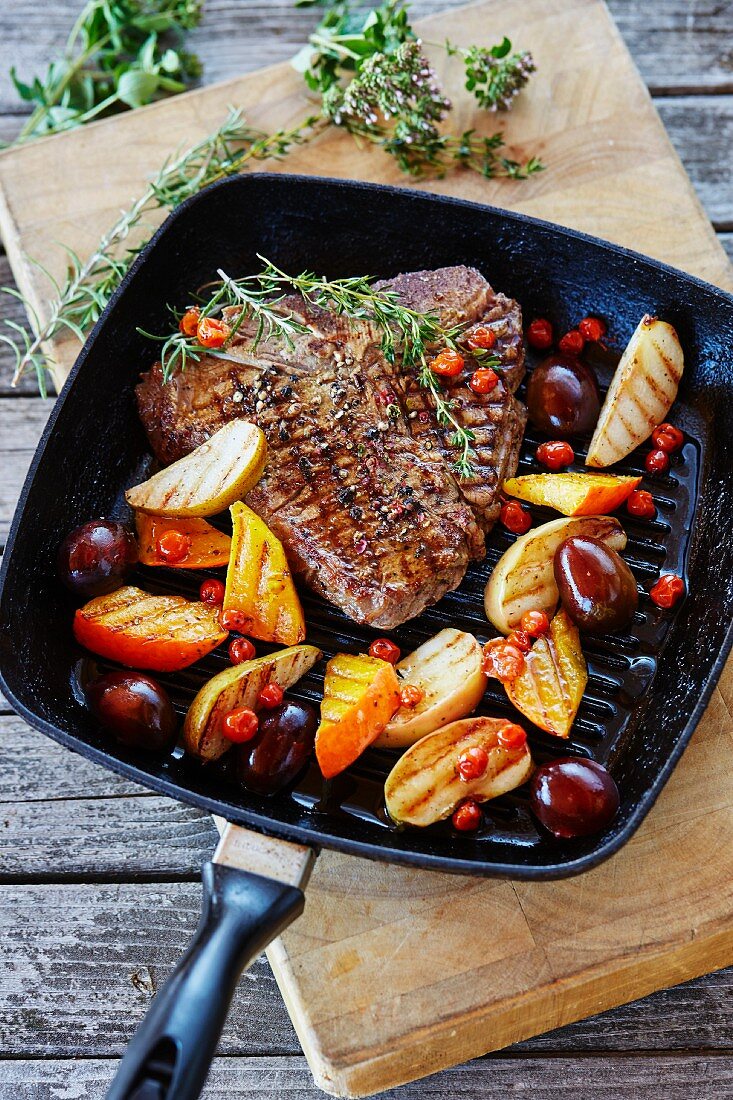 A T-bone steak wth glazed fruits and pumpkin in a grill pan