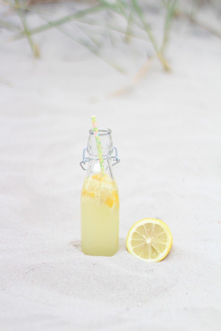 A bottle of lemonade with a lemon in the sand