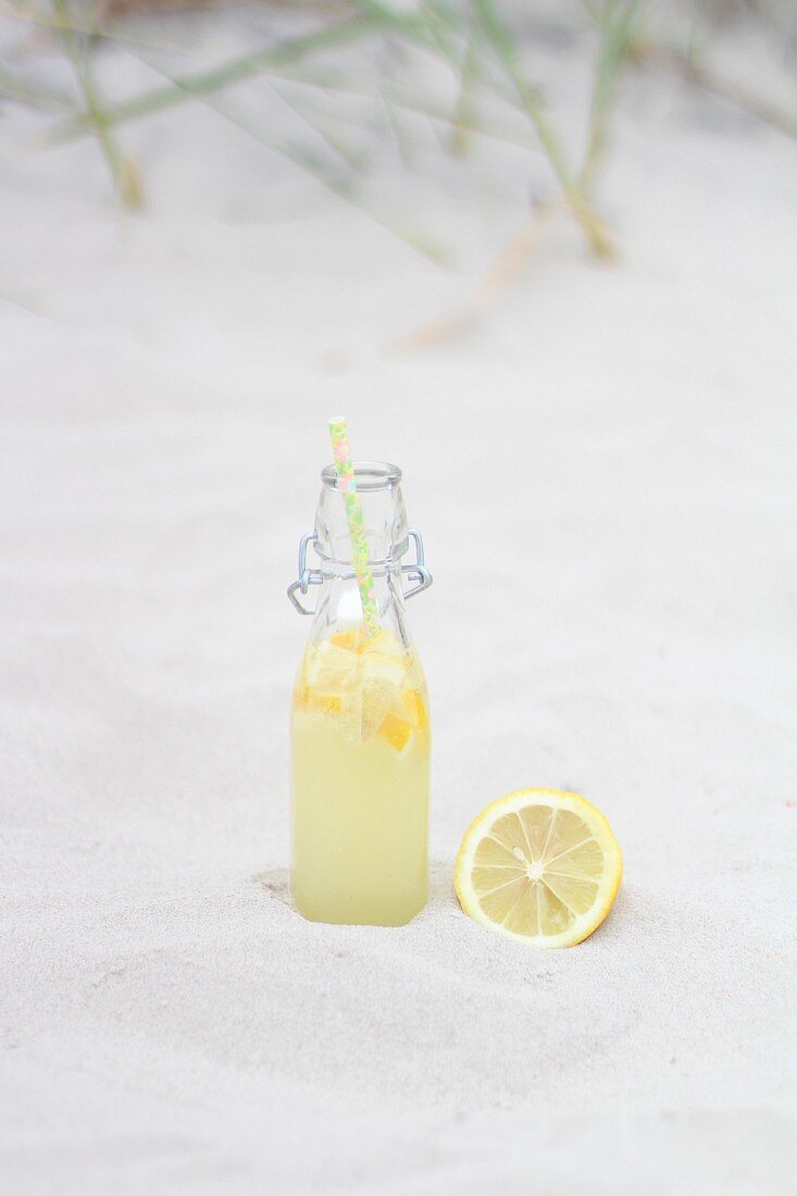 Limonadenflasche mit Zitrone im Sand