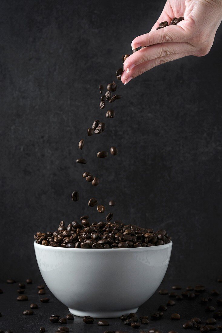 A hand throwing coffee beans into a bowl