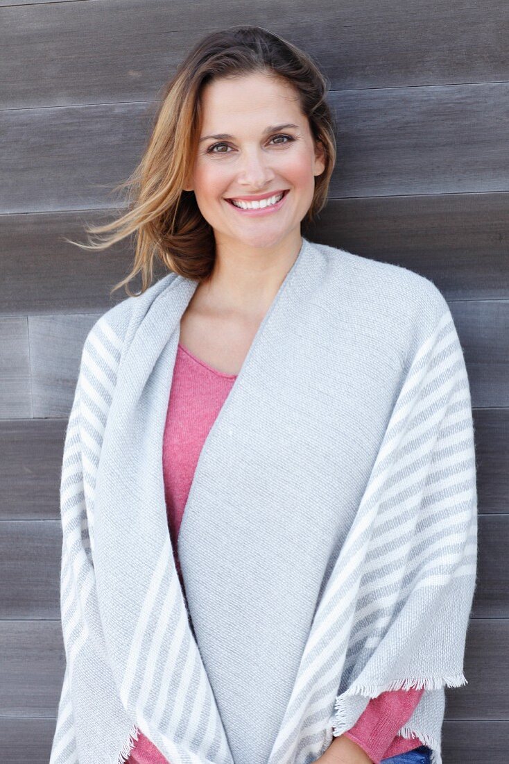 A blonde woman wearing a pink jumper with a striped blanket over her shoulders