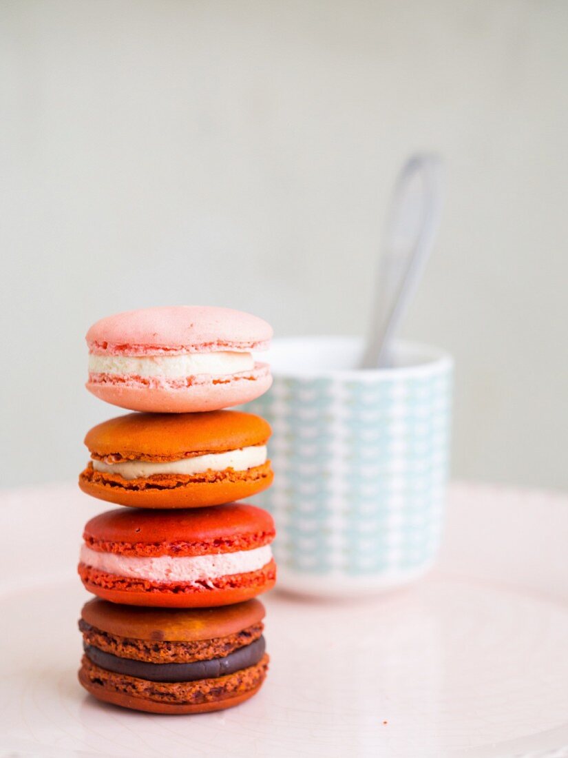 A pile of macarons in front of a cup of coffee