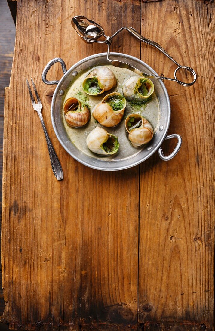 Bourgogne Escargot Snails with garlic herbs butter in aluminum pan on rustic wooden background