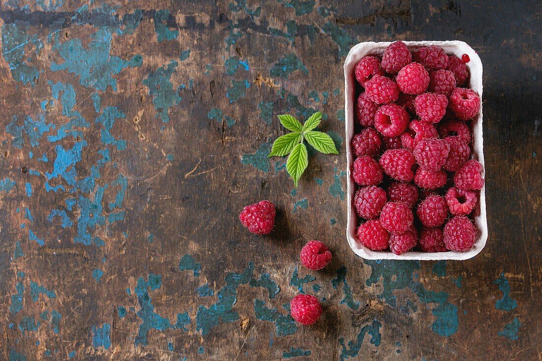 Paper market box of fresh raspberries with leaves over old wooden textured background