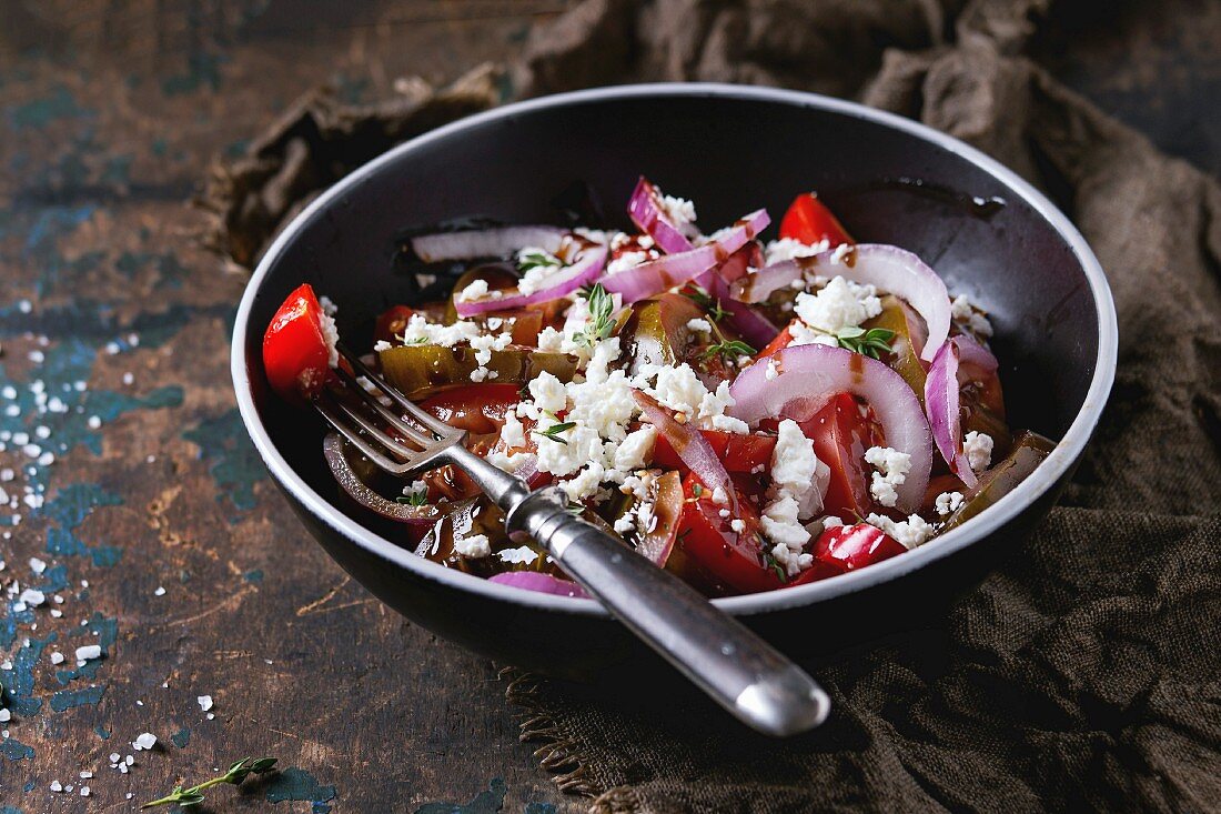 Black bowl with sliced different tomatoes, red onion, balsamic sause, thyme and feta cheese salad
