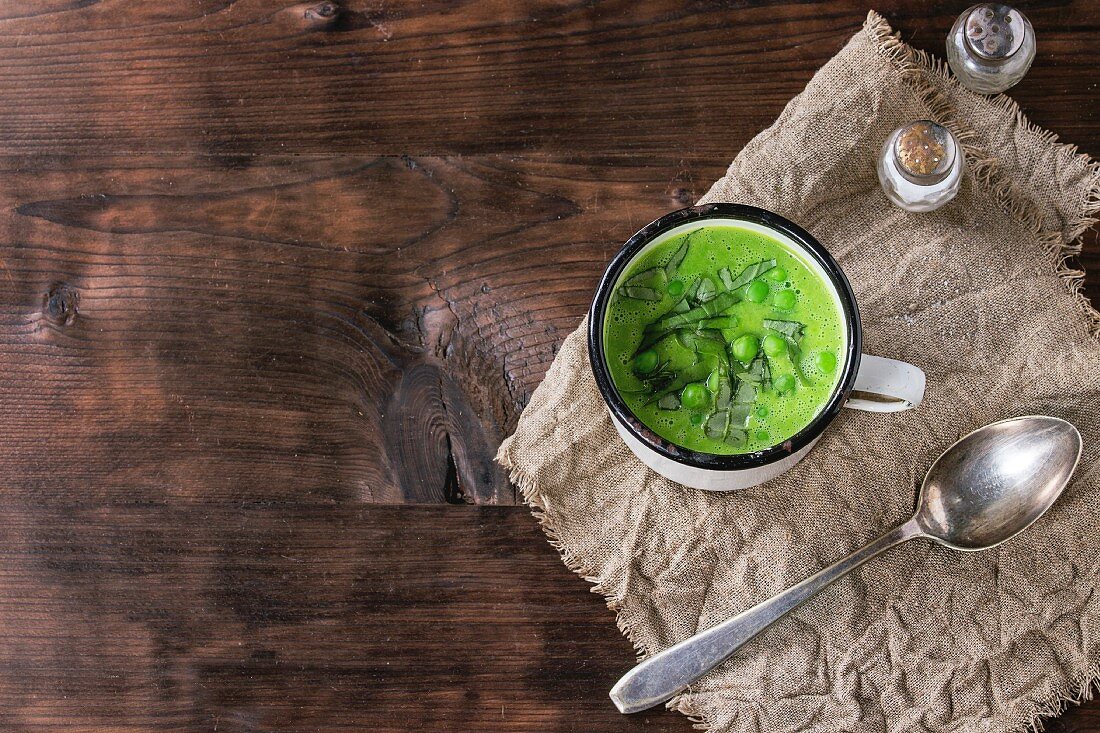 Erbsencremesuppe mit Basilikum, serviert in Vintage Becher auf Leinentuch